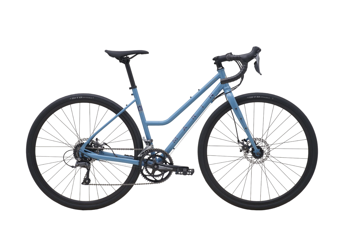 Vélo gravel urbain à cadre ouvert Marin Nicasio 1 ST 2025, coloris Blue, en vue latérale complète. On y voit le cadre en acier chromoly à double épaisseur, le cintre drop évasé et les pneus WTB Exposure 700x36c.